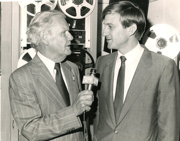 Arthur Wilkins holds a microphone as he speaks to Jeff Kennett with magnetic reels in the background