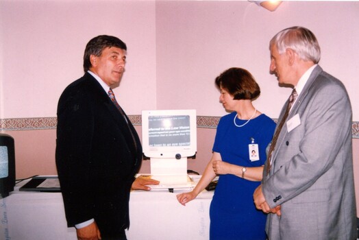 Rob Knowles stands beside computer screen with magnifier displayed at clinic