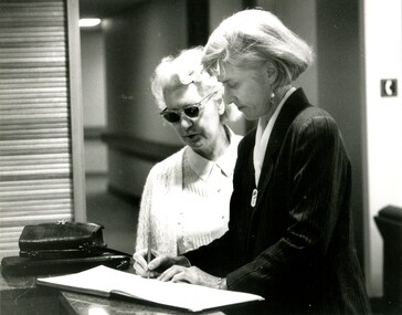 Woman signing in guest book with another beside her