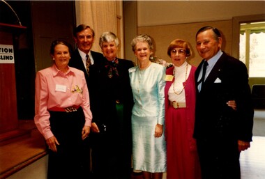 Six people stand alongside a stage in a hall