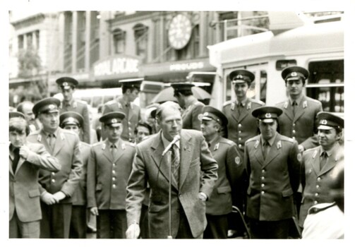 John Blanch speaks into a microphone with the Russian Male Choir behind him