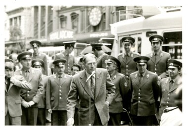 John Blanch speaks into a microphone with the Russian Male Choir behind him