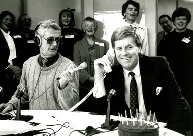 Mal Walden on telephone with cake in front of him and people singing