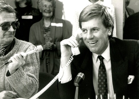 Mal Walden on telephone with cake in front of him and people singing