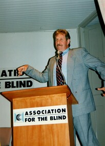 Max Walker addressing the audience from the podium with elaborate gestures