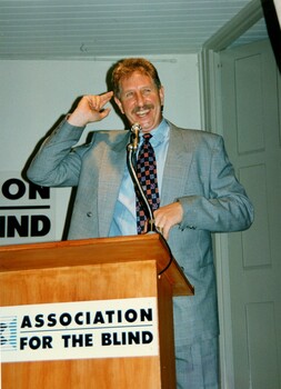 Max Walker addressing the audience from the podium with elaborate gestures