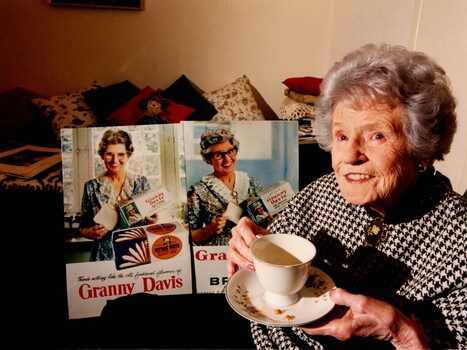 Older woman with cup of tea next to advertisements she featured in
