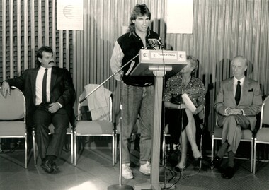 Speaker at podium whilst John Wicking and others look on