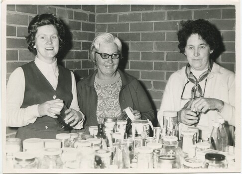 Three women filling empty jars on a table
