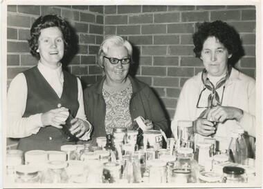 Three women filling empty jars on a table