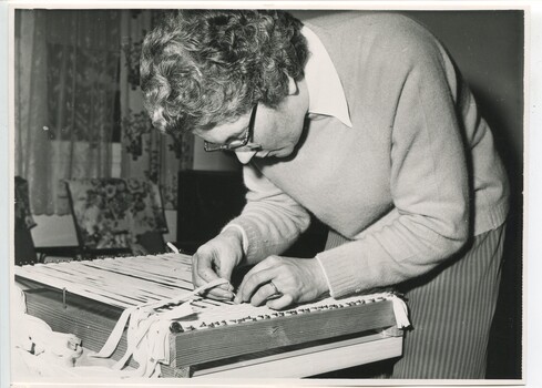 Female weaves cloth strips on to a wooden frame