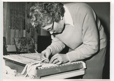 Female weaves cloth strips on to a wooden frame