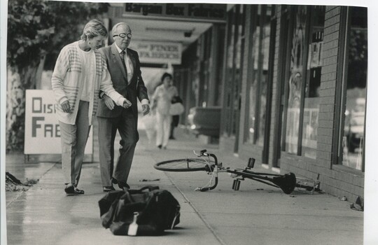 Female guiding older male around obstacles on footpath