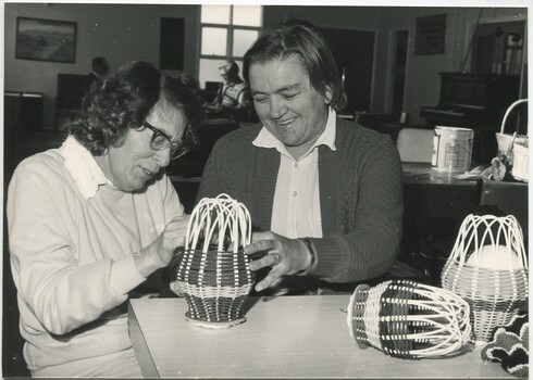Woman making a small woven cage, whilst another holds it in place
