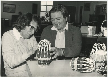 Woman making a small woven cage, whilst another holds it in place