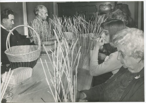 Group of people sit at a table making baskets