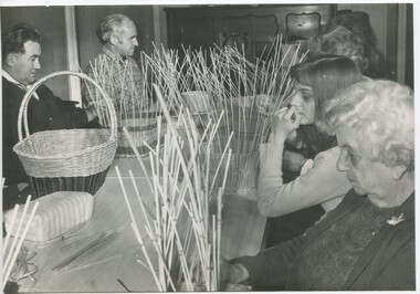 Group of people sit at a table making baskets