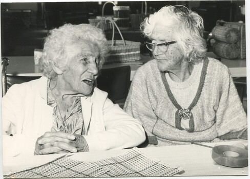 Two women chat whilst weaving looms sit in front of them