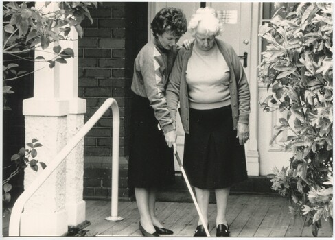 Staff member holds the white cane down for an older lady about to step down