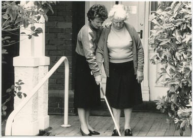 Staff member holds the white cane down for an older lady about to step down