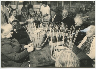 People sit around a table weaving baskets