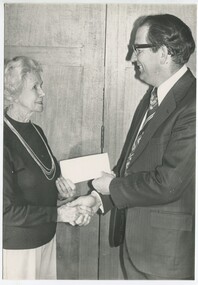 Woman presents a cheque and shakes hands with a male