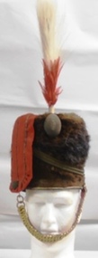 A soldier's hat with a tall feather on the top and metal chinstrap. 