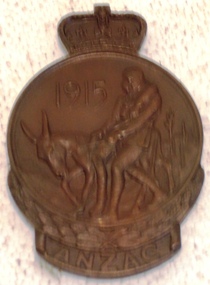 Small metal badge with sculpture on face.