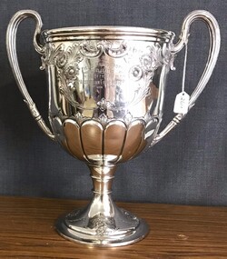 Ornate silver cup with handles and engraving on side.