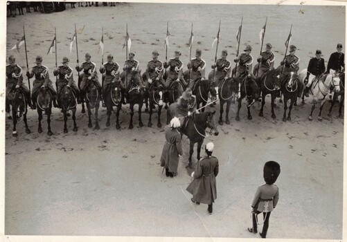 Men wearing bearskin hats inspecting line of soldiers on horses.