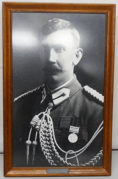 Framed photograph of army officer with plated cord around shoulder, no hat.