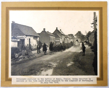 Photograph mounted on thick card of soldiers in a village