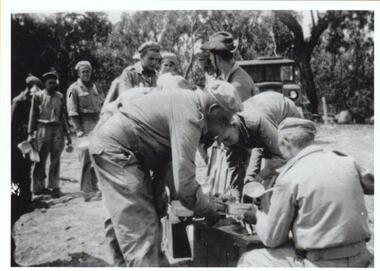 group of soldiers lined up for food in bush setting.