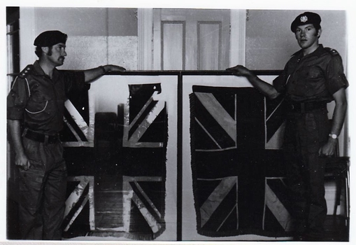 Two soldiers standing beside a frame containing two flags .