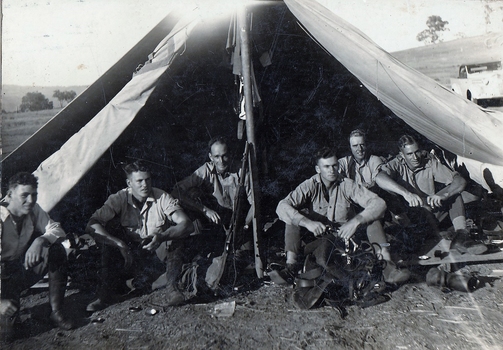 Six soldiers sitting in tent.