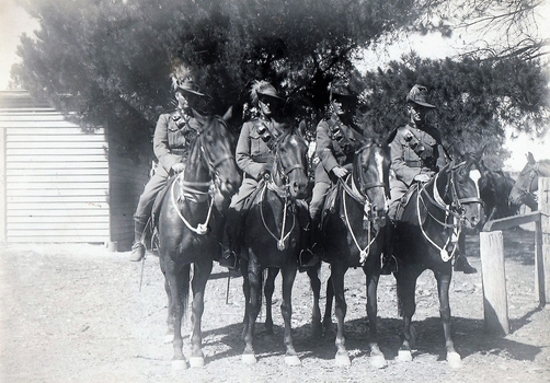 Four soldiers on horseback near fence.