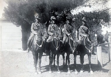 Four soldiers on horseback near fence.