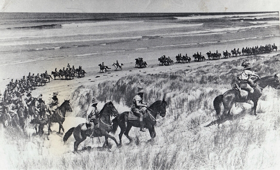 Long line of horsemen riding through sand dunes.