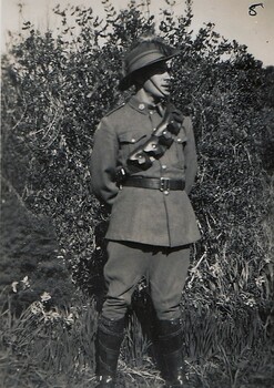 Soldier in uniform standing near tree.