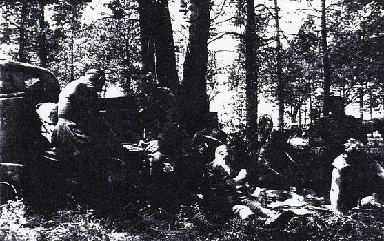 Soldiers resting under trees near car