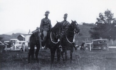 Two soldiers on horses, cars in background