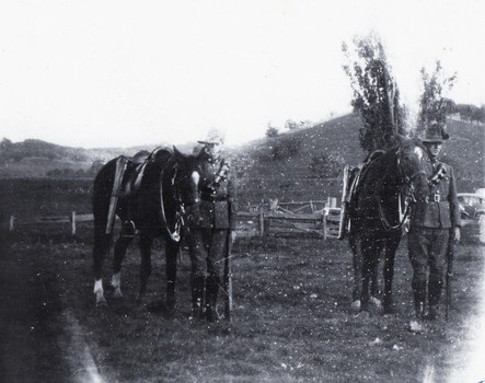 Two soldiers with horses in a fenced yard.