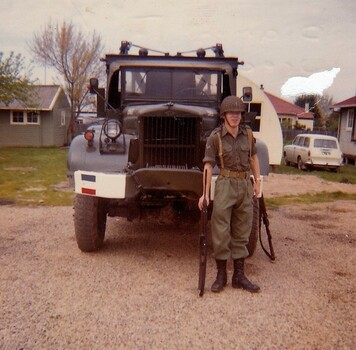 Soldier wearing helmet standing near truck.