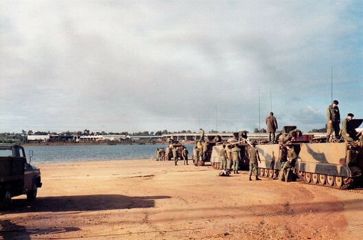 Line of Army tanks on edge of lake or sea.