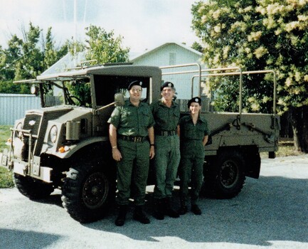 Three soldiers standing beside truck.