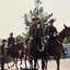 Soldiers on horseback all holding swords on a parade ground.