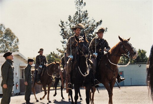 Soldiers on horseback all holding swords on a parade ground.