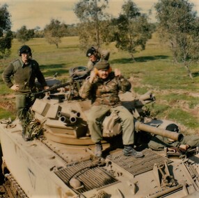 Three soldiers sitting on top of tank.