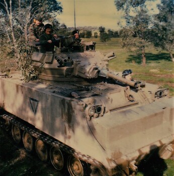 Tank in bushland with crew visible.
