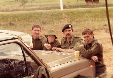 Four soldiers eating sandwiches and drinking tea.
